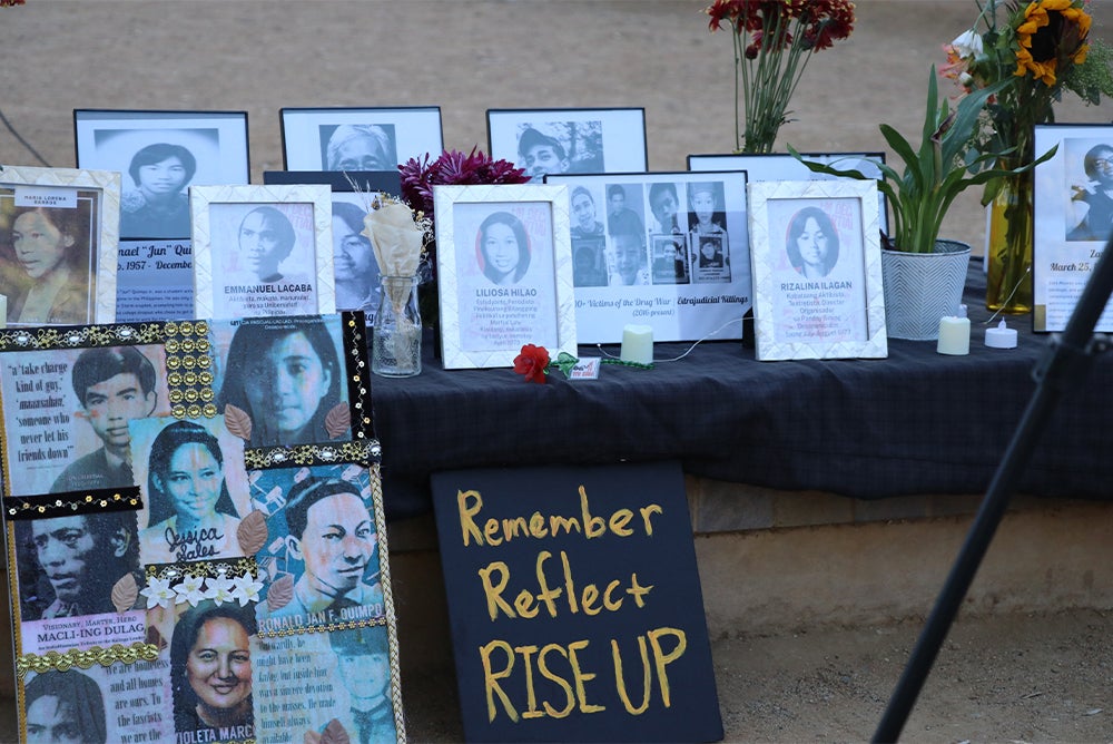 An altar with framed photos of martyrs and heroes who opposed martial law under Ferdinand E. Marcos Sr.’s and similar policies under Rodrigo Duterte. A black sign with golden yellow words "Remember Reflect RISE UP" leans against the table.