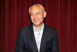 John Matsusaka in a black suit staring slightly to the left with a smile.