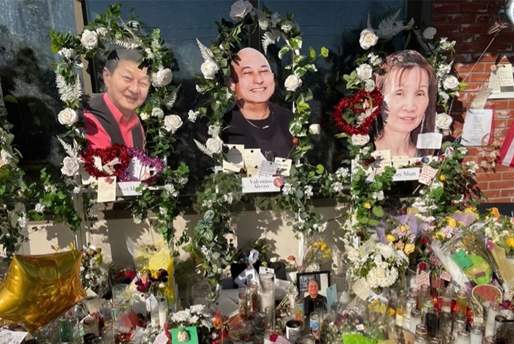 An altar to the victims of the Monterey Park shooting. Flowers, candles, small pictuers, and notes fill the table. Above the altar are three larger photos of three different victims, framed with flowers.