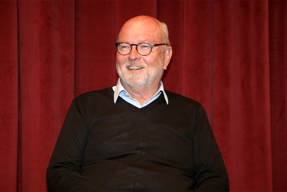 Nathan Gardels wearing a black sweater and black-rimmed glasses stares slightly to the left with his mouth open slightly to smile.