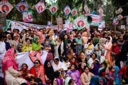 A tight crowd of men and women, some sitting down, some standing. Political banners and pictures are seen above the people.