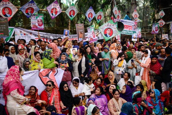 A tight crowd of men and women, some sitting down, some standing. Political banners and pictures are seen above the people.