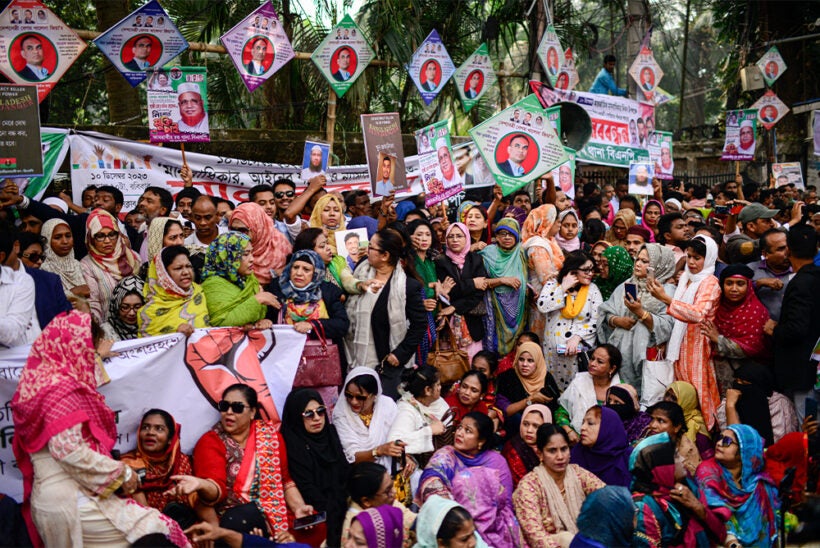 A tight crowd of men and women, some sitting down, some standing. Political banners and pictures are seen above the people.