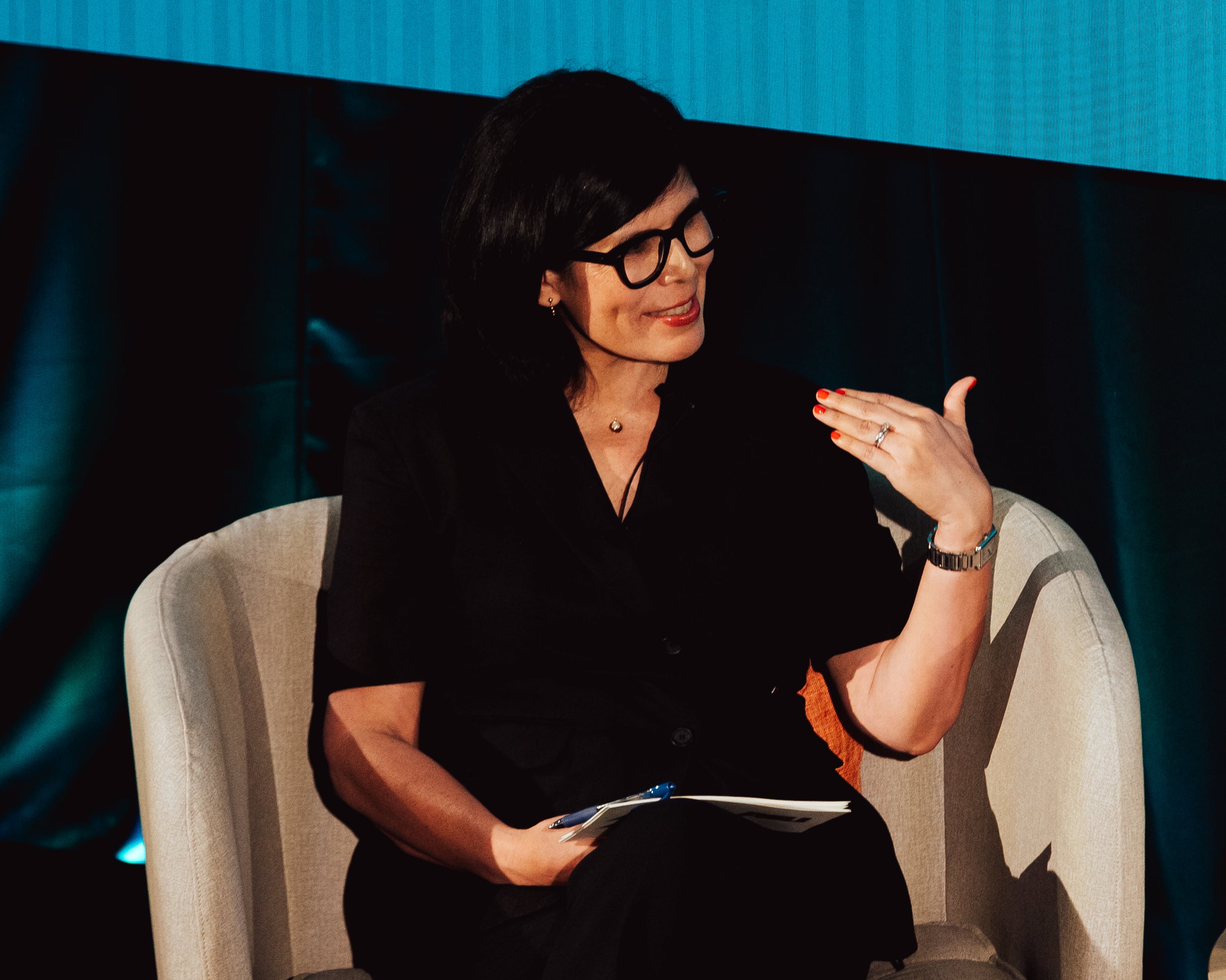 Natalia Molina, a woman with black-rimmed glasses smiles toward someone off to the side.