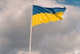 Ukraine's national flag on a flagpole swaying in the wind against slightly dark clouds.
