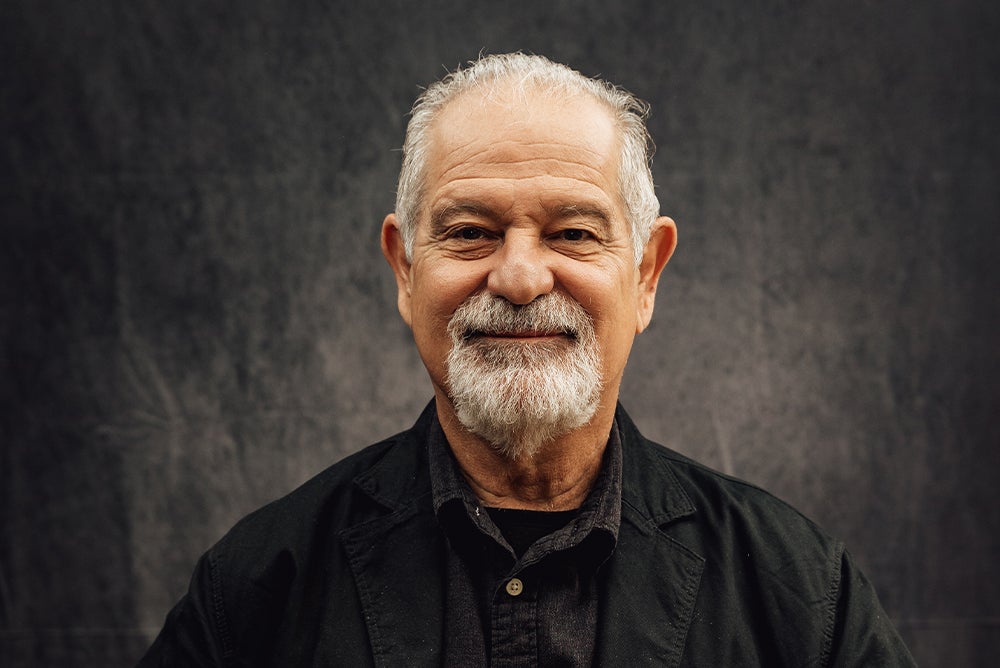 A headshot ofVíctor Zúñiga smiling against a gray-black backdrop. He wears a dark navy shirt.